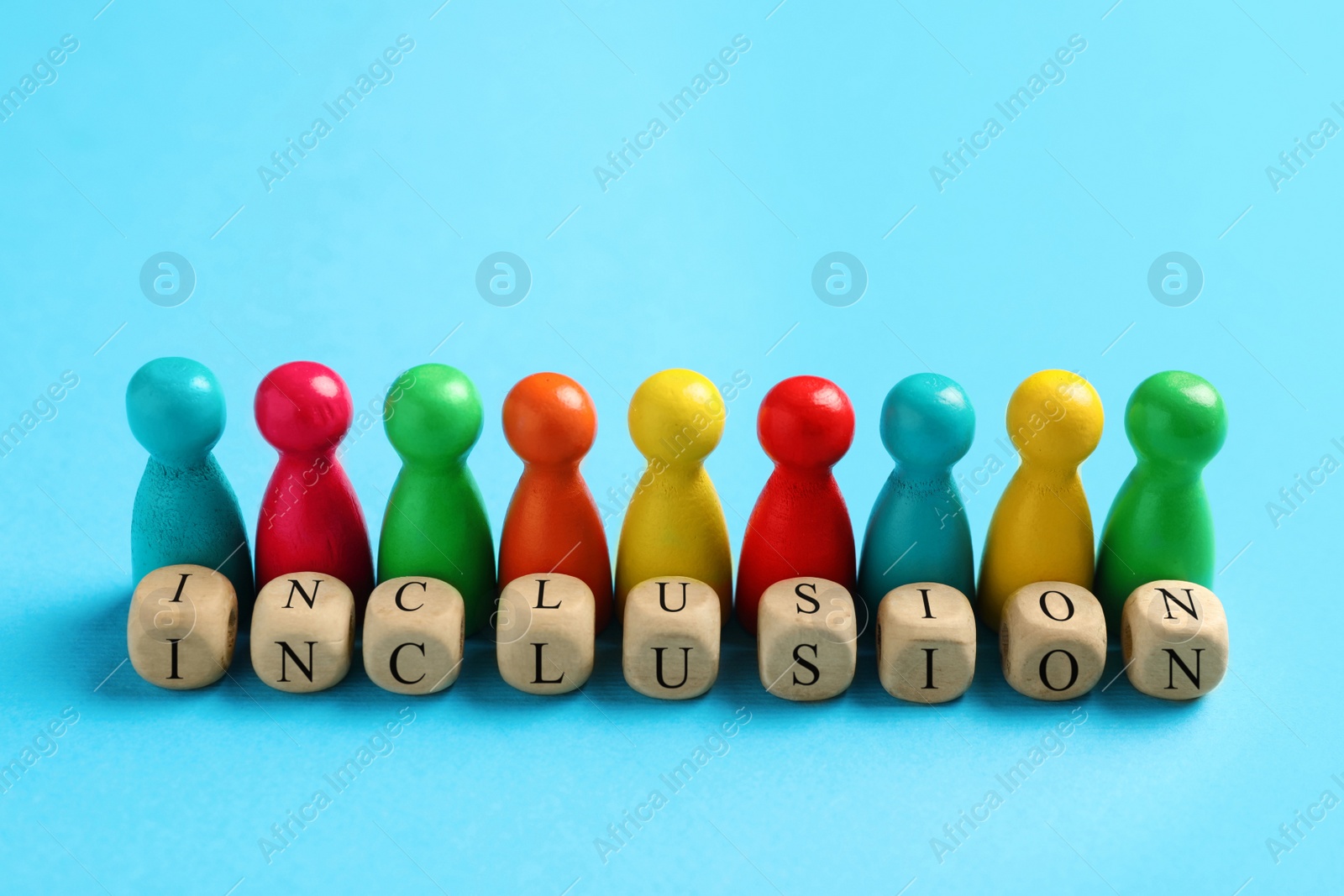 Photo of Colorful pawns and wooden cubes with word Inclusion on light blue background