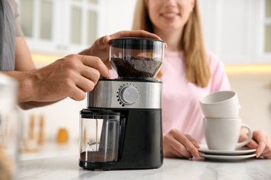 Couple together in kitchen. Man using electric coffee grinder, closeup