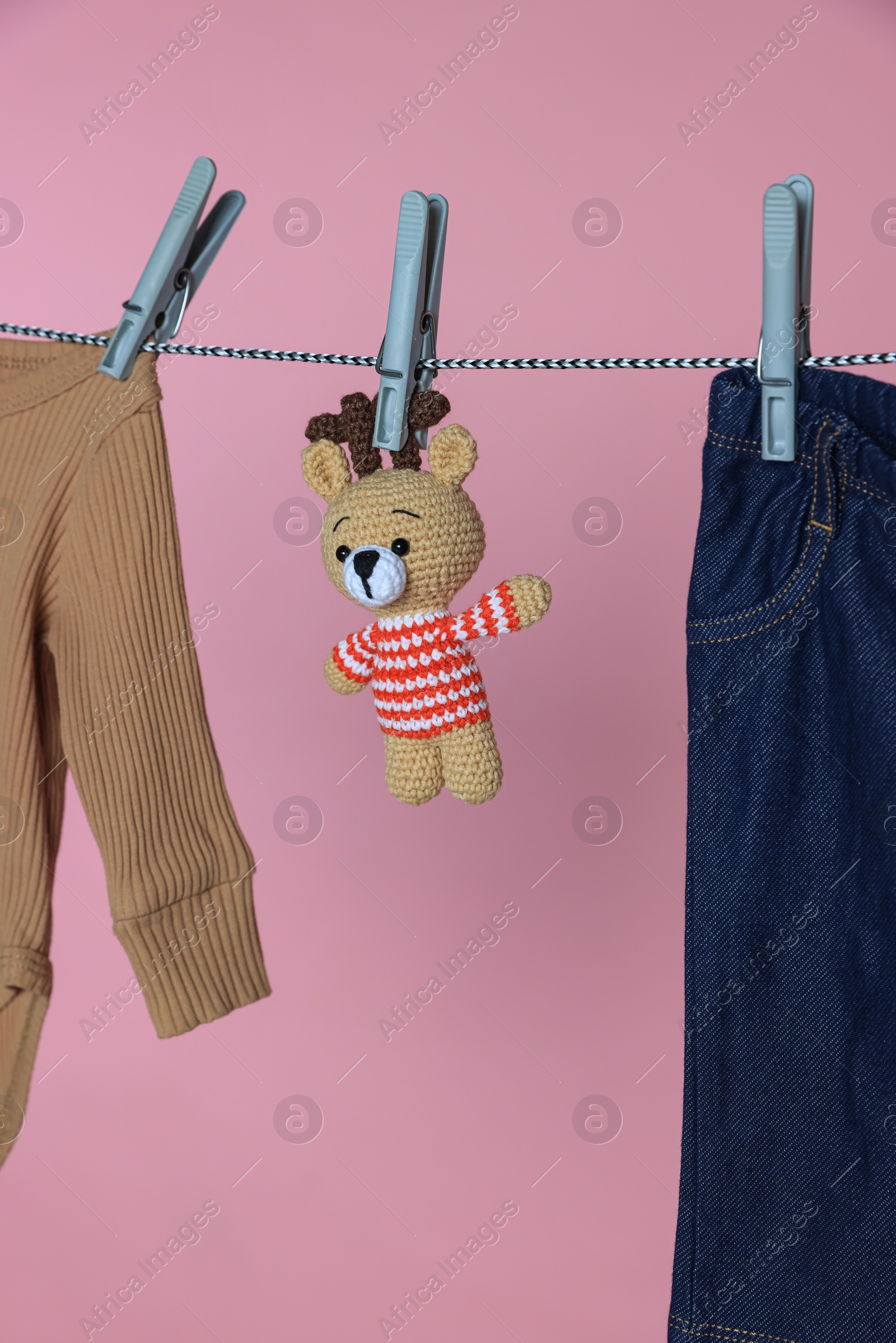 Photo of Different baby clothes and bear toy drying on laundry line against pink background