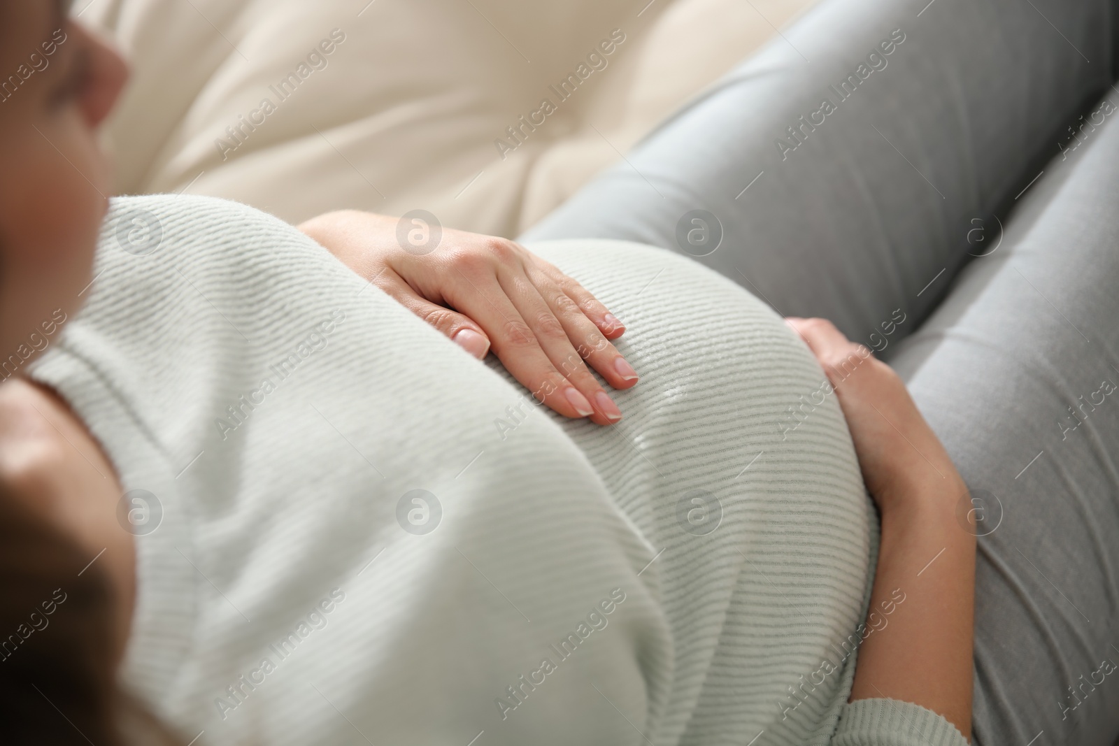 Photo of Pregnant woman touching her belly indoors, closeup