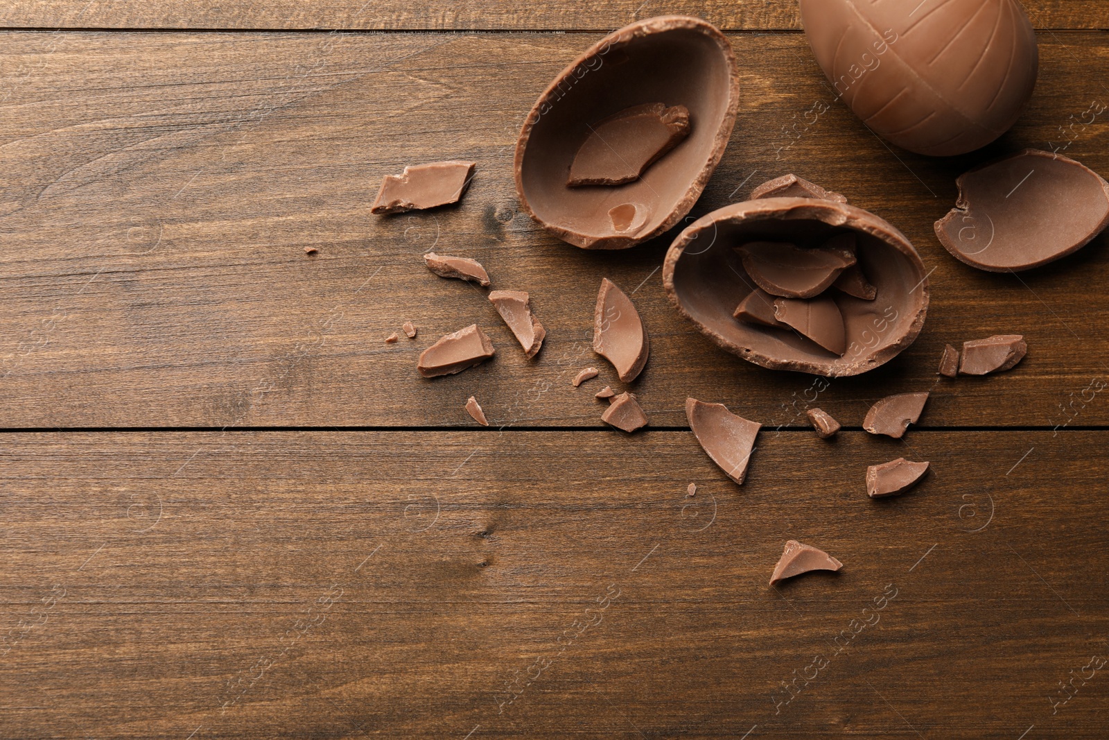 Photo of Broken and whole chocolate eggs on wooden table, flat lay. Space for text