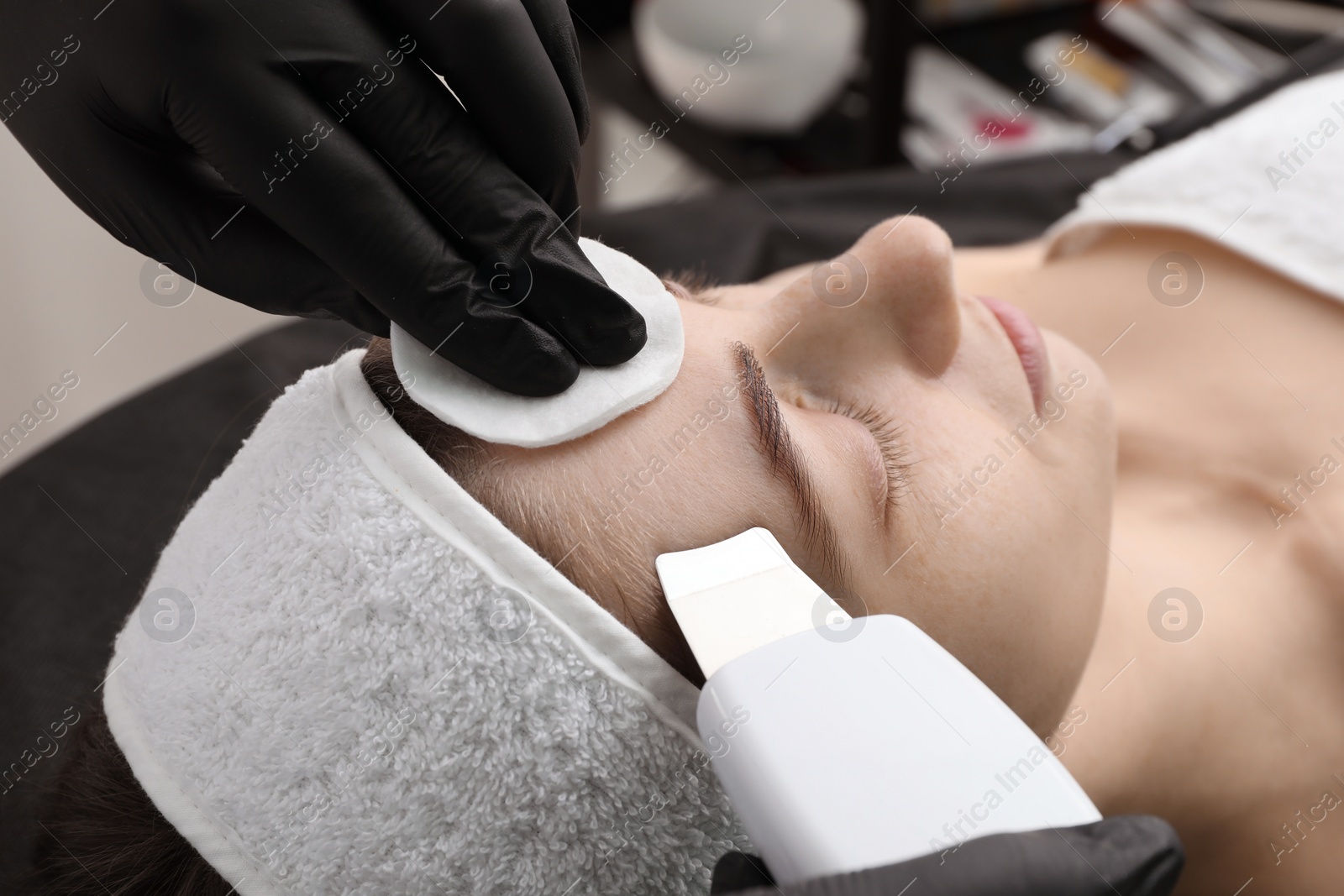 Photo of Cosmetologist using ultrasonic scrubber, closeup. Client having cleansing procedure indoors