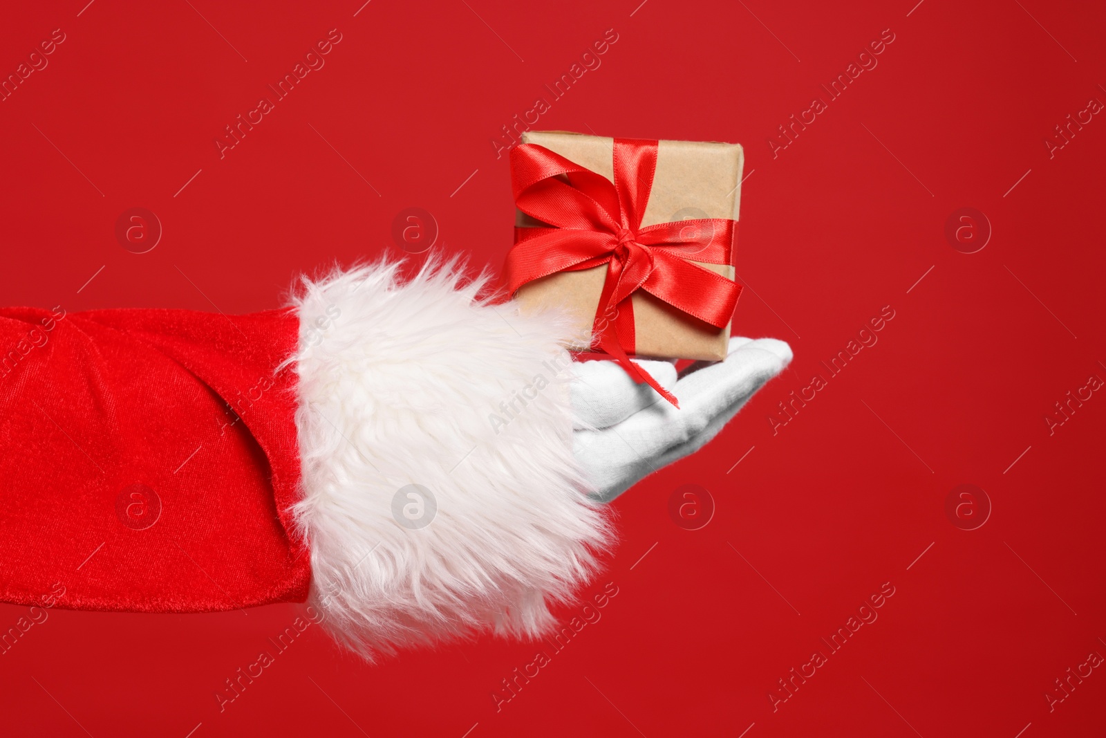 Photo of Santa Claus holding Christmas gift on red background, closeup