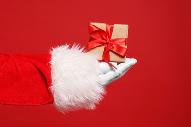 Santa Claus holding Christmas gift on red background, closeup