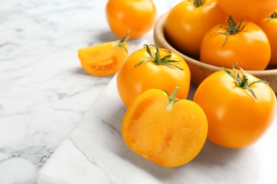 Photo of Ripe yellow tomatoes on white marble table, closeup. Space for text