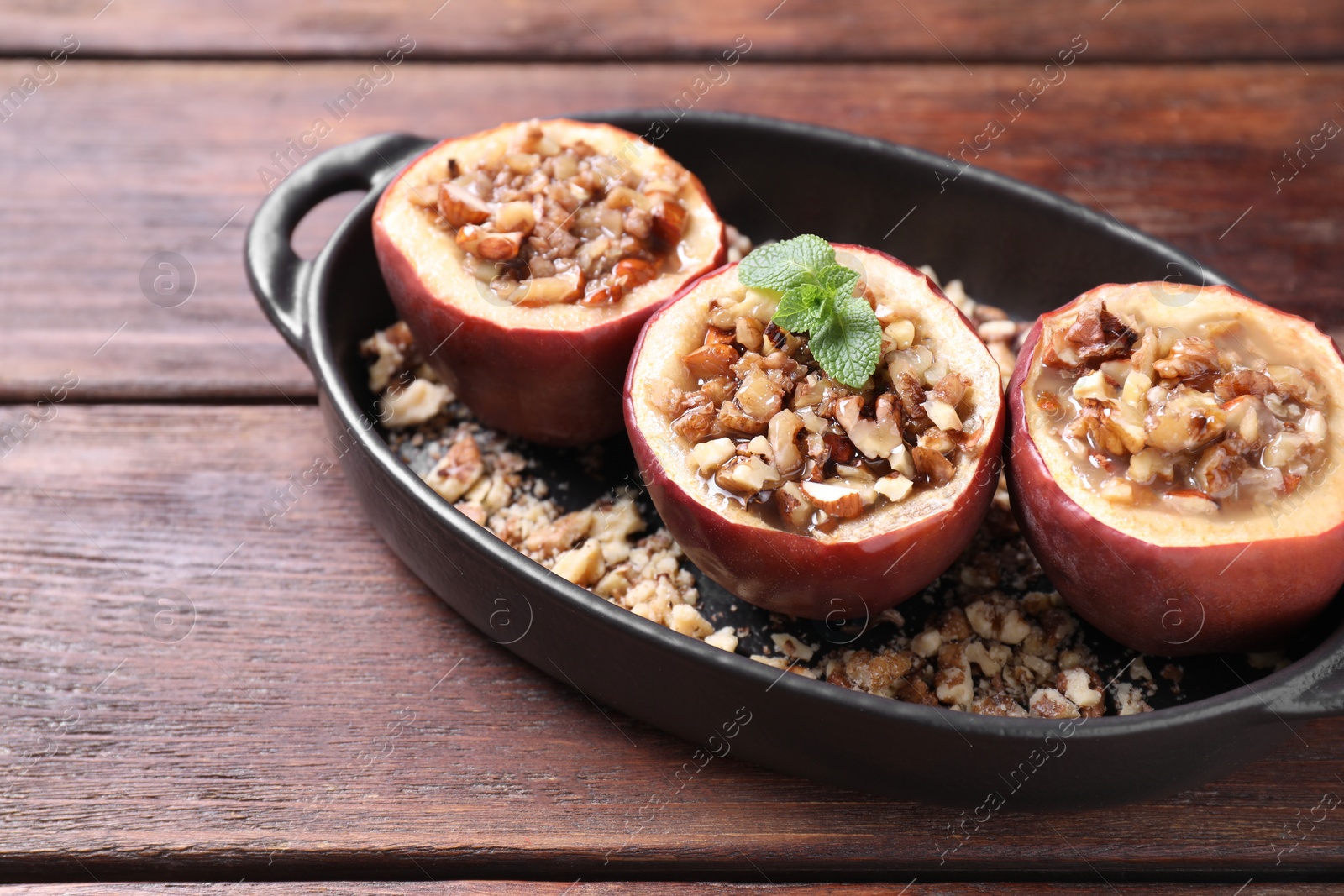 Photo of Tasty baked apples with nuts, honey and mint in baking dish on wooden table, closeup