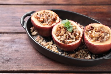 Tasty baked apples with nuts, honey and mint in baking dish on wooden table, closeup