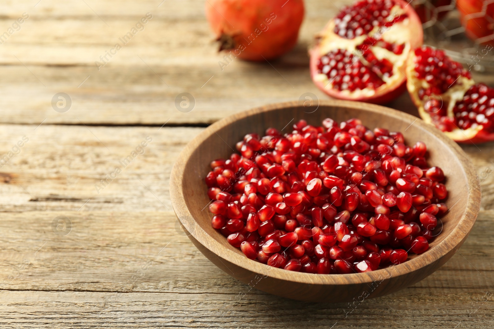 Photo of Ripe juicy pomegranate grains in bowl on wooden table. Space for text