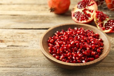 Photo of Ripe juicy pomegranate grains in bowl on wooden table. Space for text