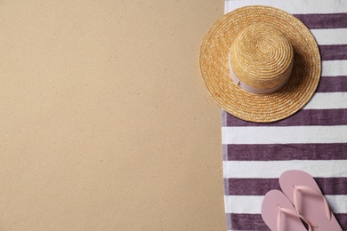 Photo of Straw hat, flip flops and space for text on beach sand, top view. Summer vacation