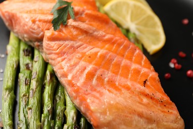 Tasty grilled salmon with asparagus and spices on plate, closeup