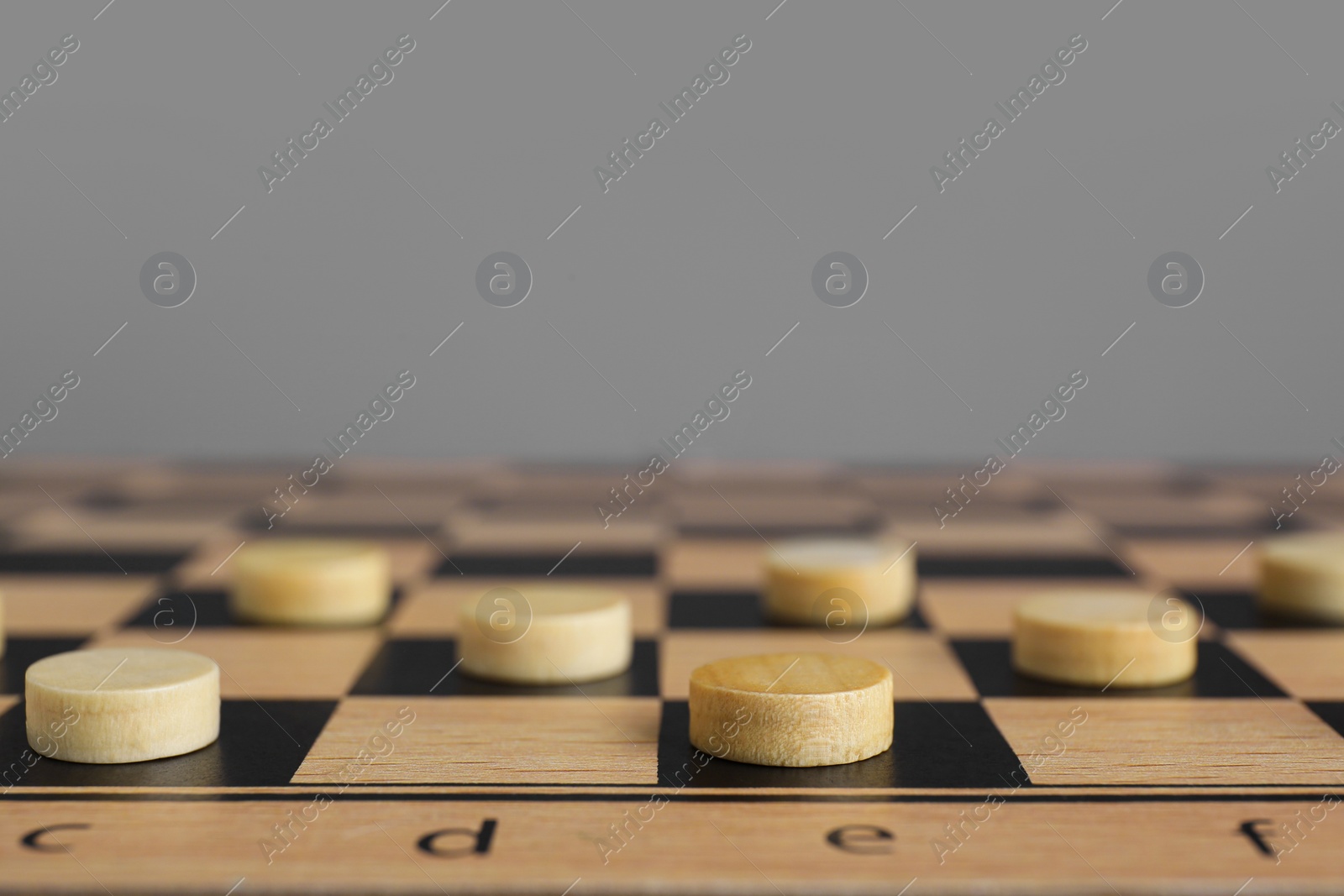 Photo of Wooden checkerboard with game pieces on light grey background, closeup