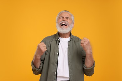 Emotional senior sports fan celebrating on yellow background