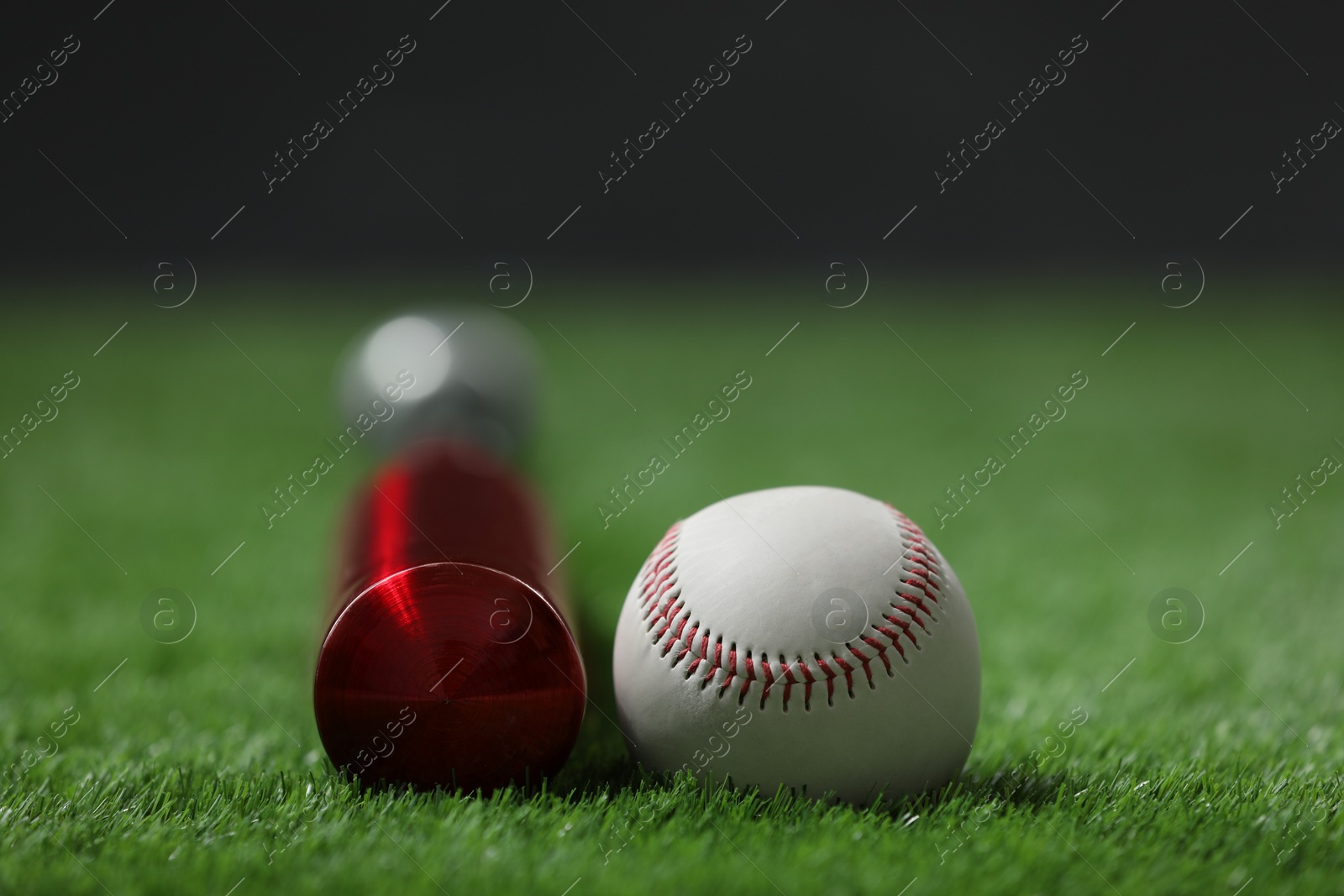 Photo of Baseball bat and ball on green grass against dark background, closeup. Space for text