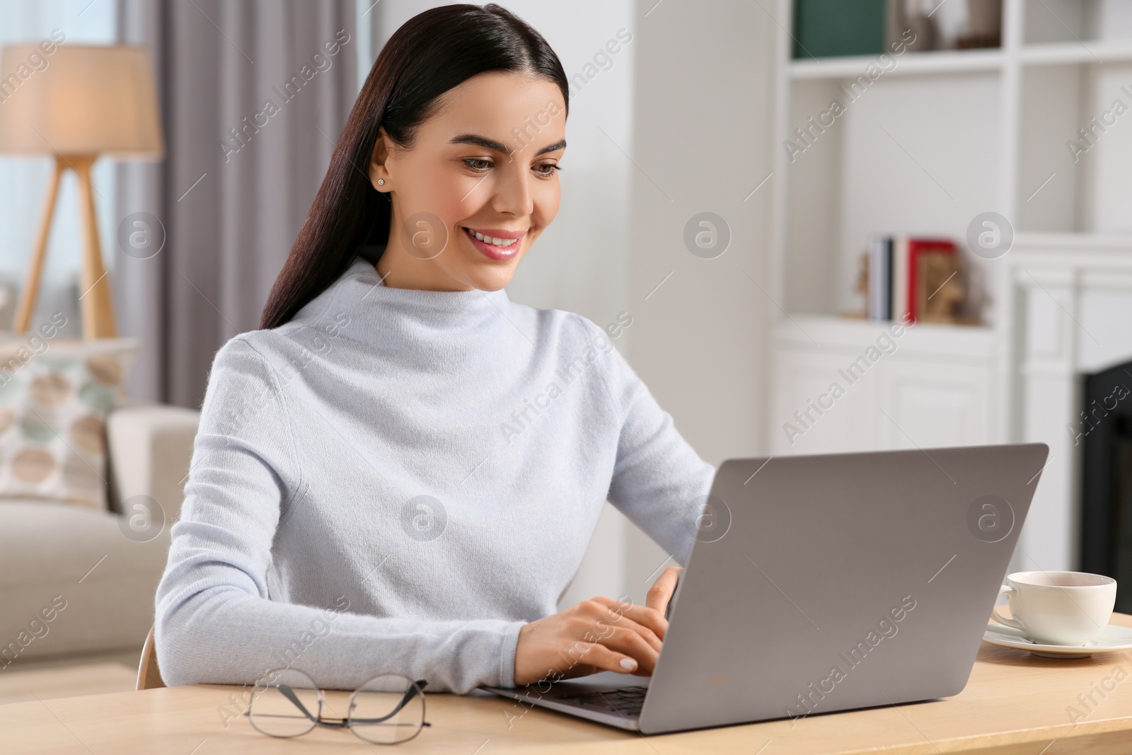 Photo of Happy woman working with laptop at wooden desk in room