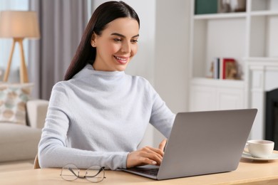 Happy woman working with laptop at wooden desk in room