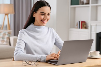 Photo of Happy woman working with laptop at wooden desk in room