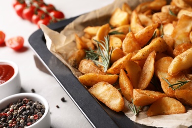 Photo of Baking sheet with potatoes and rosemary on table, closeup