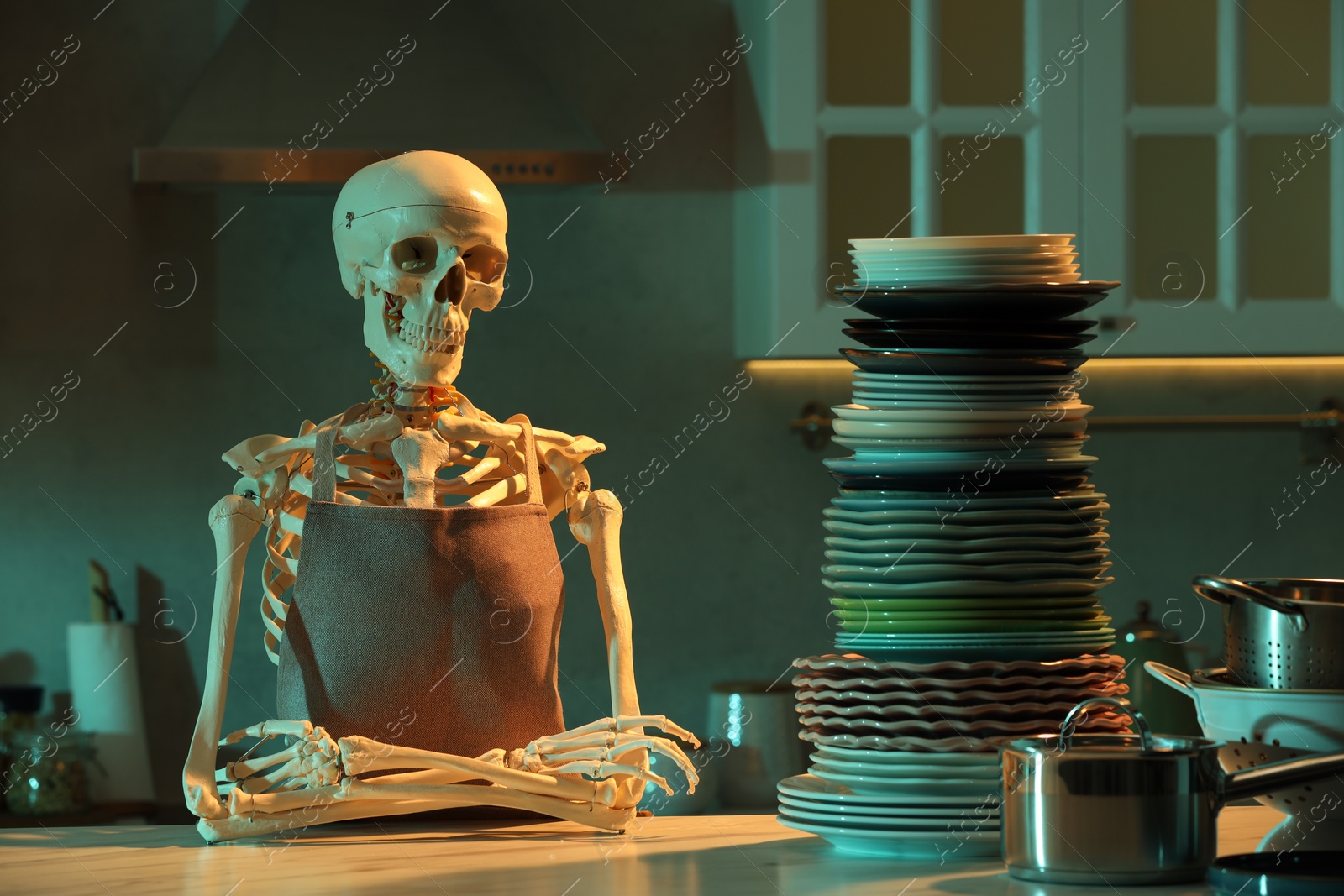 Photo of Human skeleton sitting at white marble table with clean dishware in kitchen at night