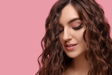 Beautiful young woman with long curly brown hair on pink background, closeup. Space for text