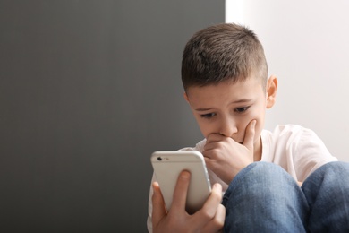 Photo of Upset boy with smartphone indoors. Space for text