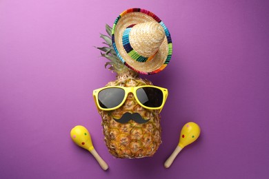 Photo of Pineapple with Mexican sombrero hat, fake mustache, maracas and sunglasses on purple background, flat lay