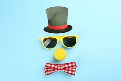 Photo of Clown face made of glasses, cylinder and bow tie on light blue background, flat lay