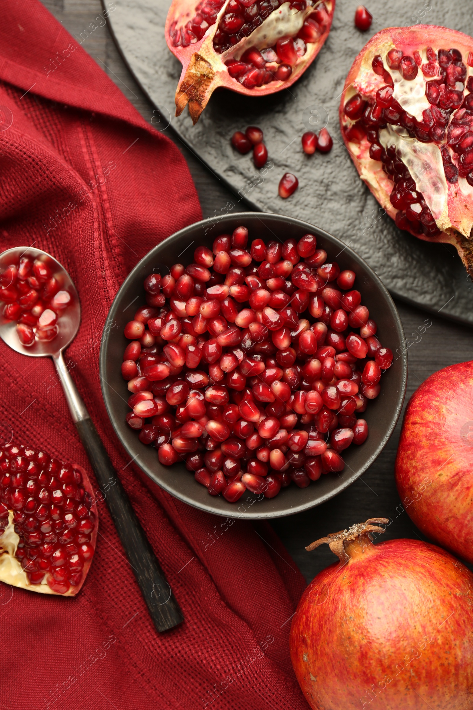 Photo of Tasty ripe pomegranates and grains on dark wooden table, flat lay