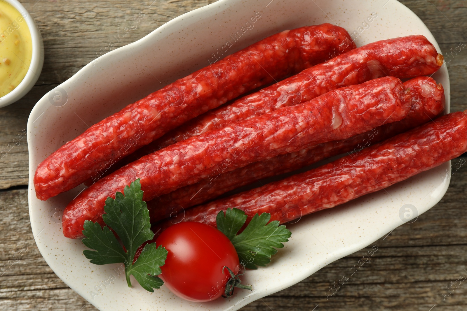 Photo of Bowl with thin dry smoked sausages, tomato and parsley on old wooden table, flat lay