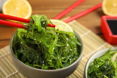 Chopsticks with Japanese seaweed salad in bowl on table, closeup