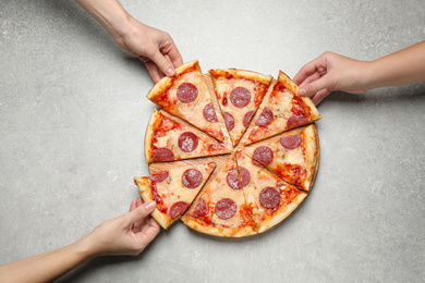 People taking slices of tasty pepperoni pizza at light grey table, top view