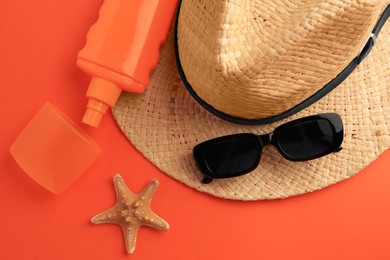 Photo of Bottle of sunscreen, starfish and beach accessories on coral background, flat lay