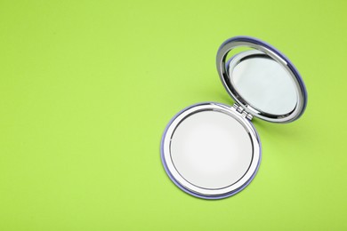 Stylish cosmetic pocket mirror on light green background, top view. Space for text