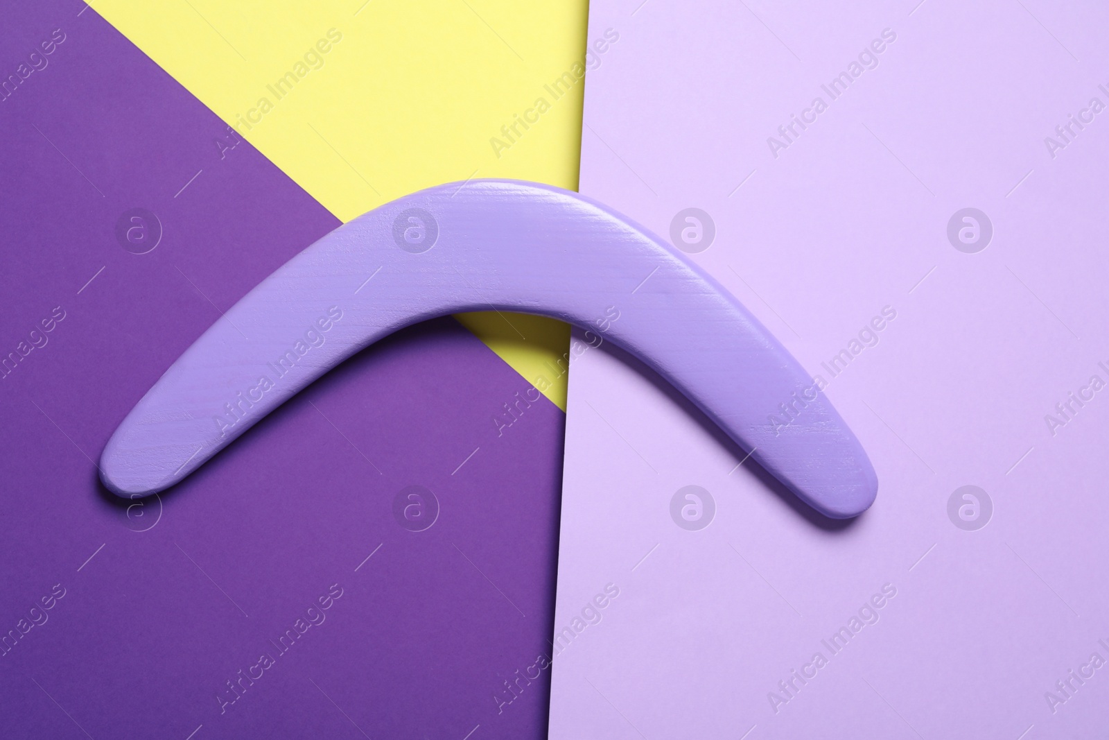 Photo of Lilac wooden boomerang on color background, top view