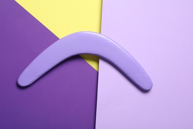 Lilac wooden boomerang on color background, top view