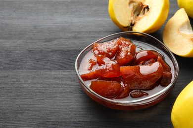 Quince jam in glass bowl and fresh raw fruits on grey wooden table. Space for text