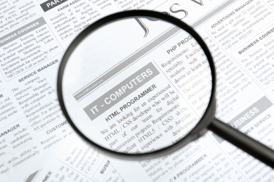 Photo of Looking through magnifying glass at newspaper, closeup. Job search concept