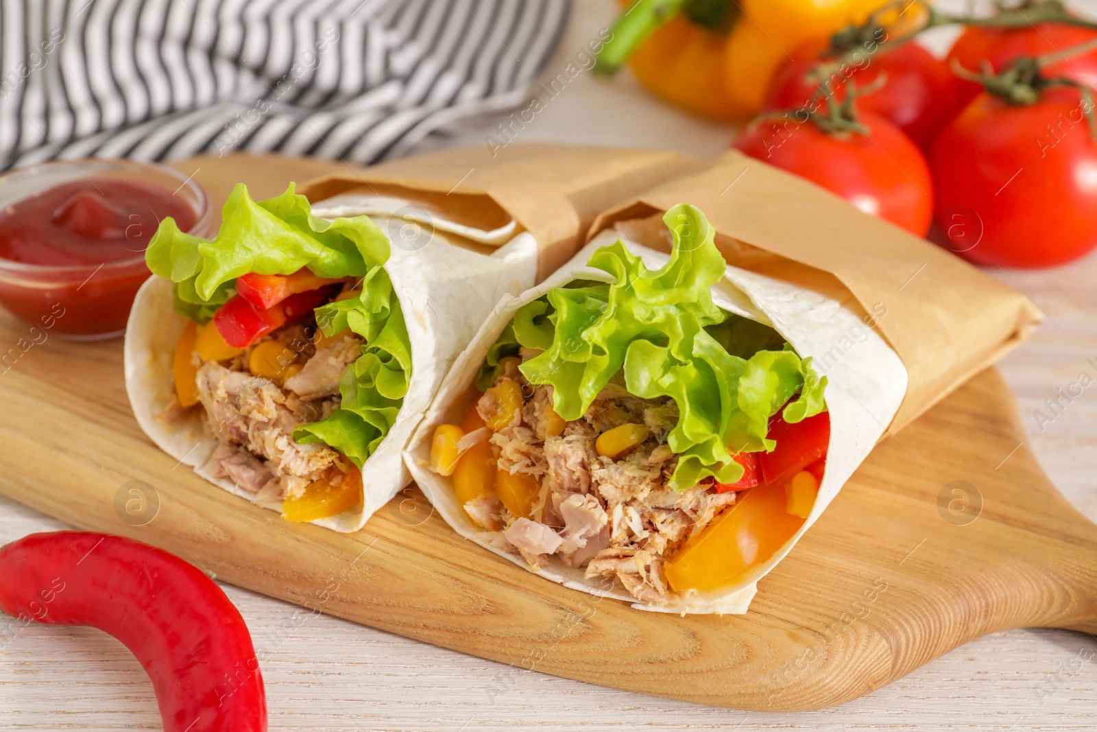 Photo of Delicious tortilla wraps with tuna on white wooden table