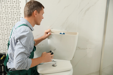 Photo of Professional plumber repairing toilet bowl in bathroom