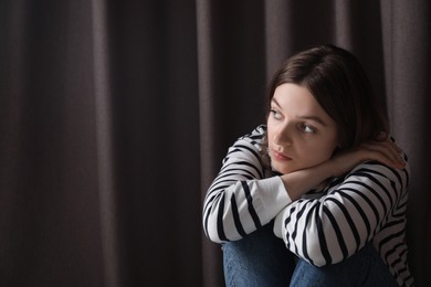 Photo of Sad young woman near curtains indoors, space for text