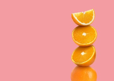 Stacked cut and whole oranges on pink background, space for text