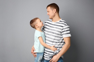 Photo of Dad and his son hugging on grey background. Father's day celebration