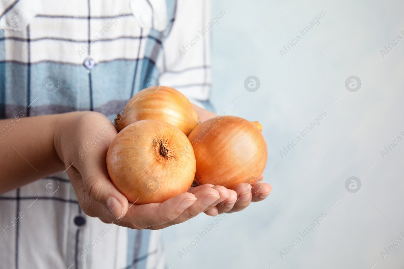 Photo of Woman holding handful of ripe onions on blue background, closeup with space for text