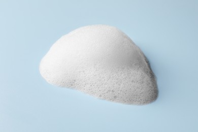 Photo of Drop of fluffy soap foam on light blue background