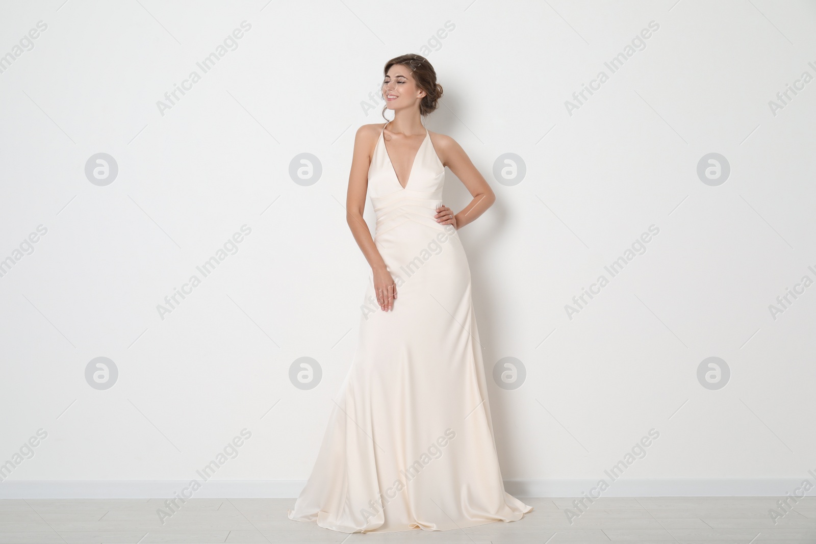 Photo of Young bride wearing beautiful wedding dress near light wall
