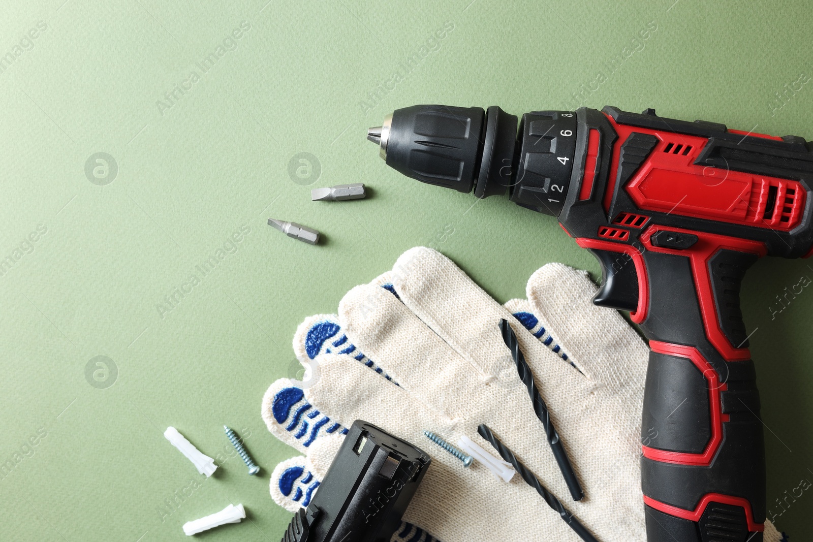 Photo of Electric screwdriver, gloves and accessories on pale green background, flat lay