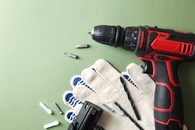 Photo of Electric screwdriver, gloves and accessories on pale green background, flat lay