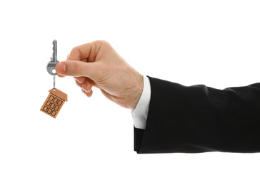 Photo of Real estate agent holding house key with trinket on white background, closeup