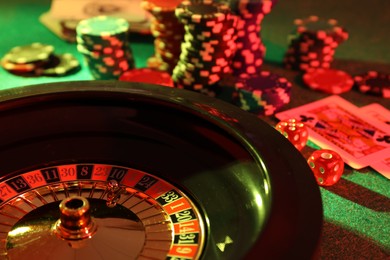 Photo of Roulette wheel with ball, playing cards and chips on green table, closeup. Casino game