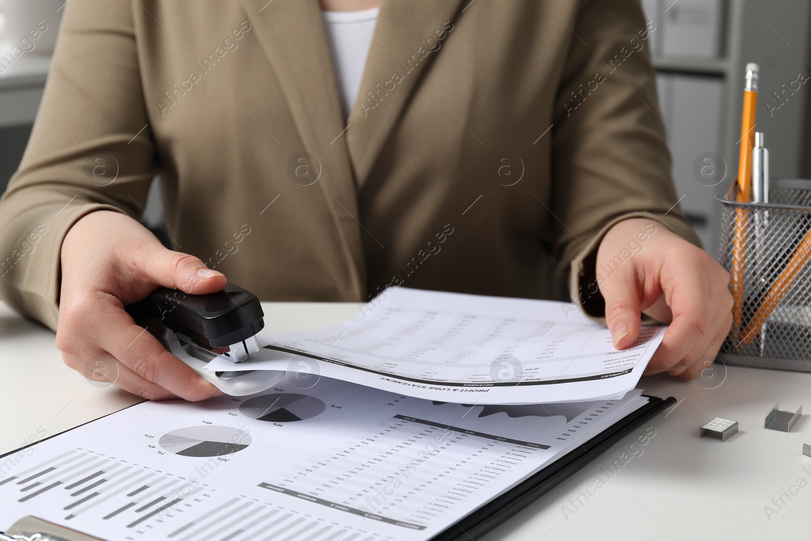 Photo of Woman stapling documents at white table indoors, closeup